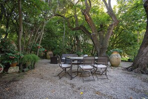 An outdoor patio with a table and chairs, surrounded by trees and potted plants. - Homerez - Villa in Saint-Rémy-de-Provence (Saint-Rémy-de-Provence)