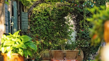 Une terrasse avec une table et des chaises en bois, entourée de plantes en pot et d’un grand jardinière.