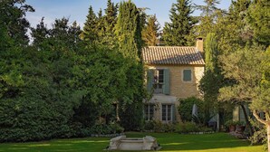 Une maison en pierre avec un toit de tuiles, entourée d’une végétation luxuriante et d’une pelouse bien entretenue.