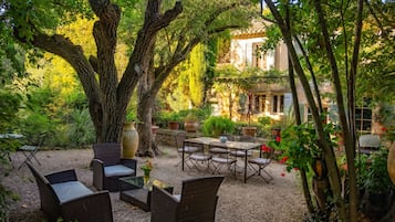 An outdoor seating area with wicker furniture, surrounded by trees and potted plants.