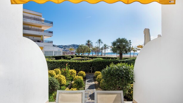 On aperçoit, à travers un auvent blanc et jaune, un jardin aménagé avec un sentier menant à un bâtiment doté de balcons.