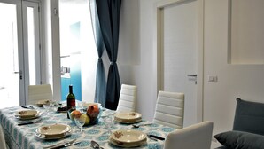 Comedor con una mesa dispuesta para cuatro, con platos, cubiertos y una botella de vino. Hay dos sillas y un sofá en la habitación.