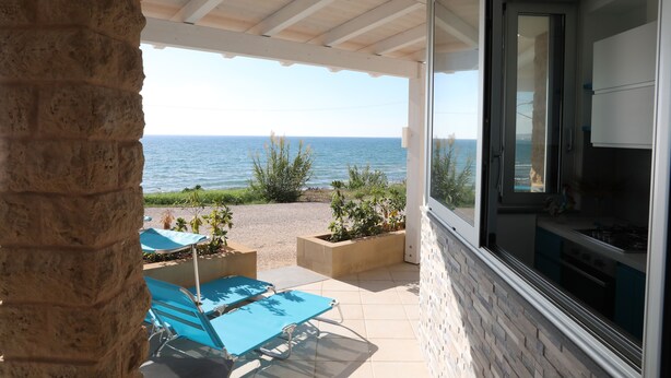 Un patio techado con vista al mar, un pilar de piedra y una zona de cocina con armarios y estufa.