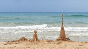 Una playa arenosa con dos esculturas de arena, una con una pelota en la parte superior y otra estructura más alta y esbelta.