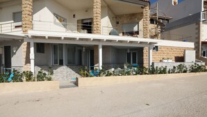 Un edificio de dos pisos con un patio cubierto, pilares de piedra y un pequeño jardín con plantas.