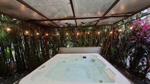 Un jacuzzi rodeado de abundante vegetación e iluminación tenue, todo bajo una cubierta metálica.