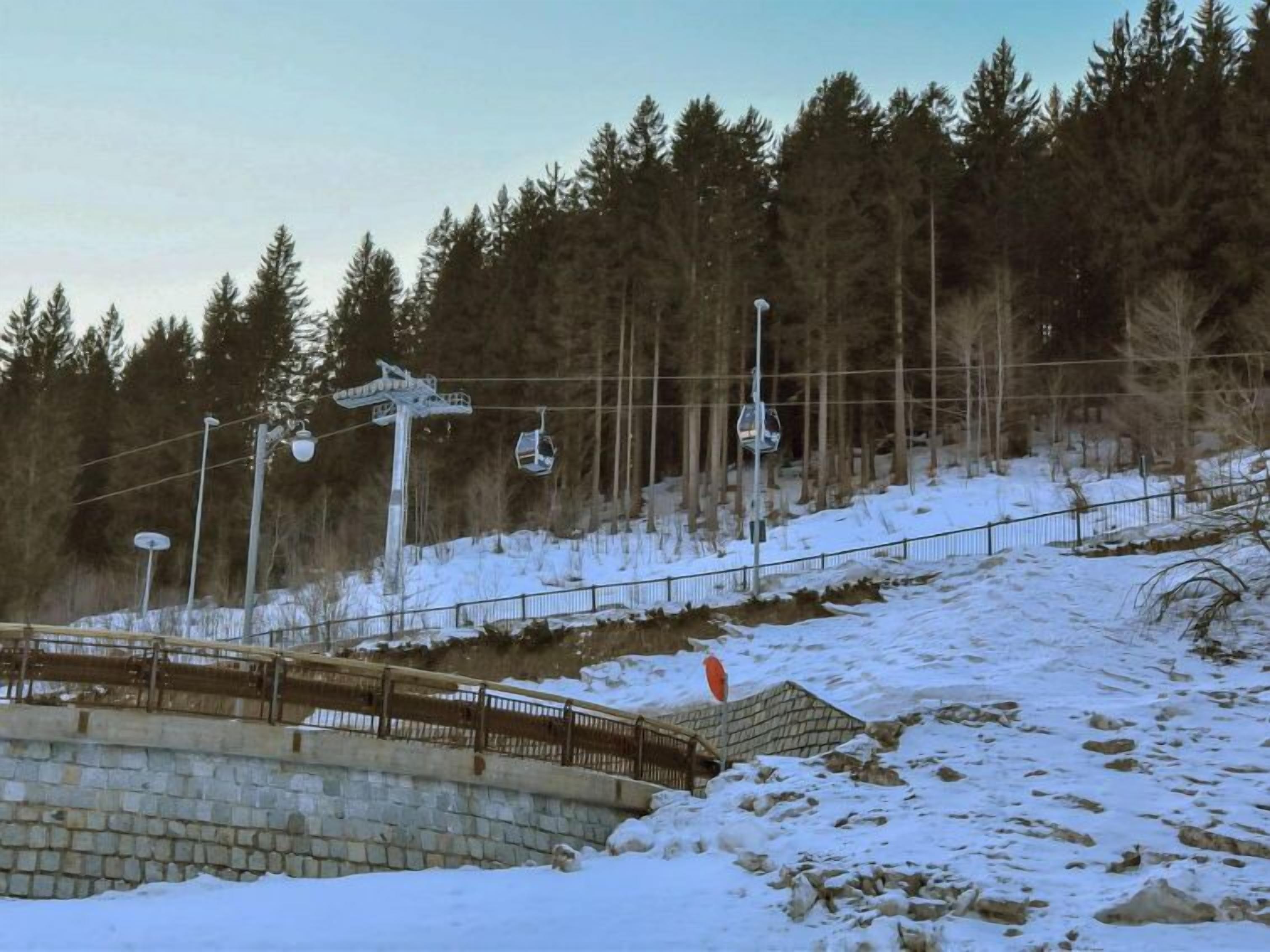 Pista de esquí nevada con un telesilla y un muro de piedra.