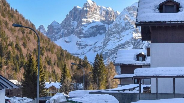Un chalet de montagne, dont le toit est recouvert de neige, entouré d’arbres et surplombant un ciel bleu et dégagé.