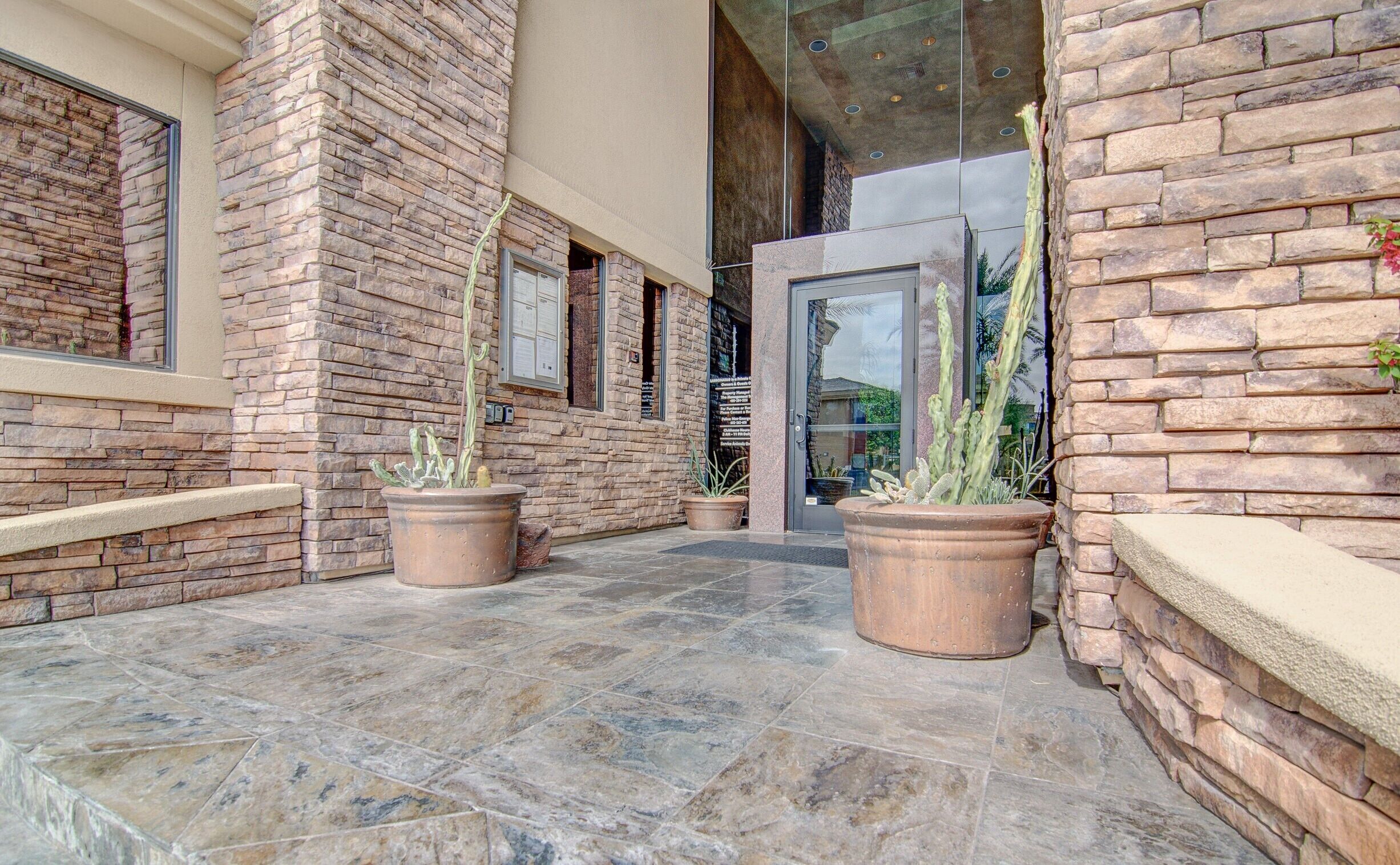 A building entrance with a stone facade, large potted cacti, and a tiled floor.