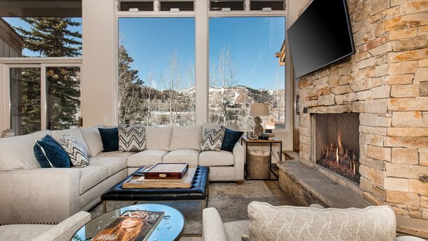 A cozy living room with a stone fireplace, a flat-screen TV, and a large window offering a mountain view. - 4 Bdr/4.5Bath-Steps to lifts and Stein Eriksen (Park City)