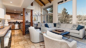 A spacious living area with a large sofa, armchairs, and a coffee table. A kitchen is visible in the background with wooden cabinets and a dining area. - 4 Bdr/4.5Bath-Steps to lifts and Stein Eriksen (Park City)