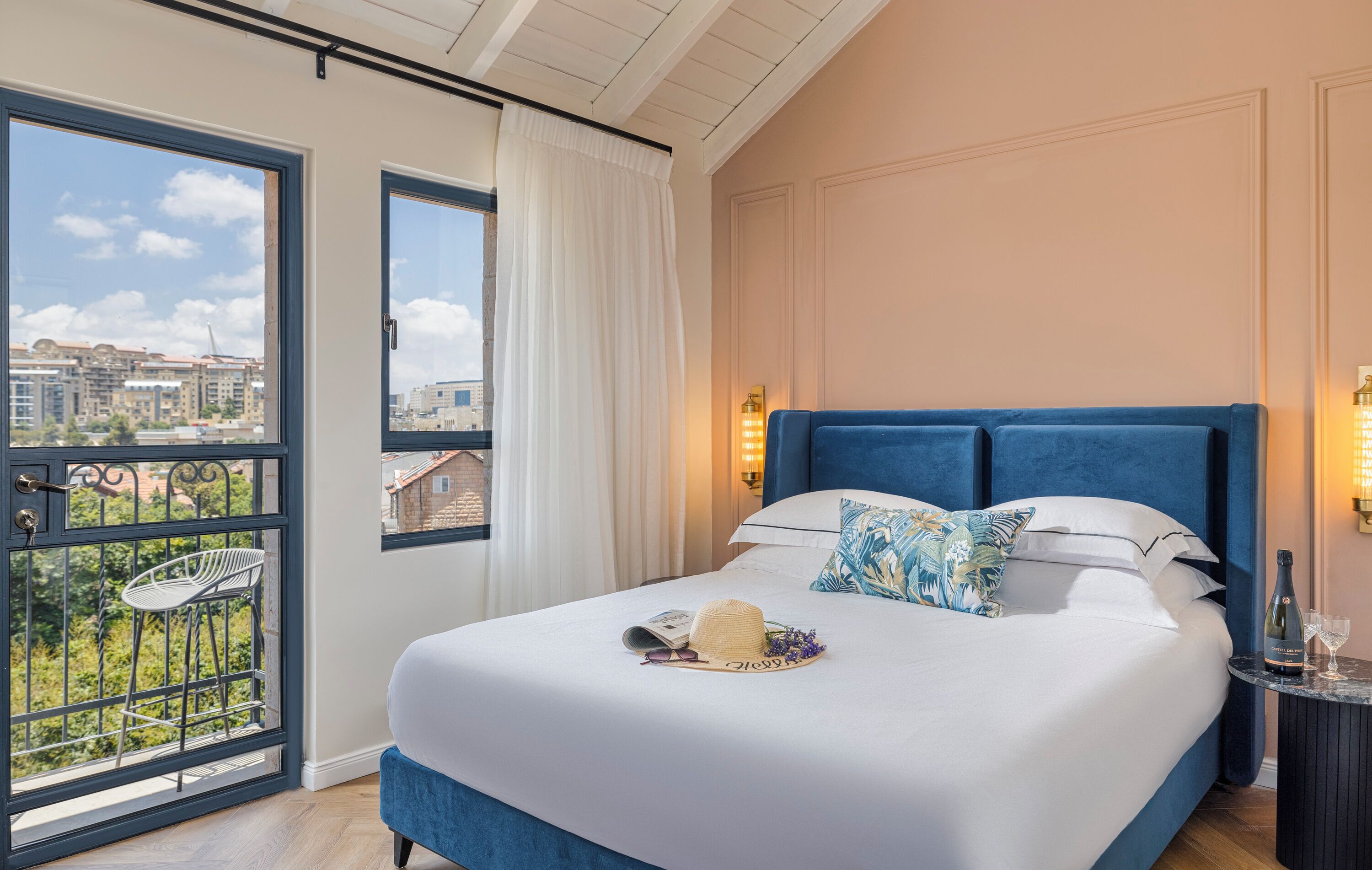 Un dormitorio con una cama grande, vistas de edificios a través de una ventana y un balcón con una silla.
