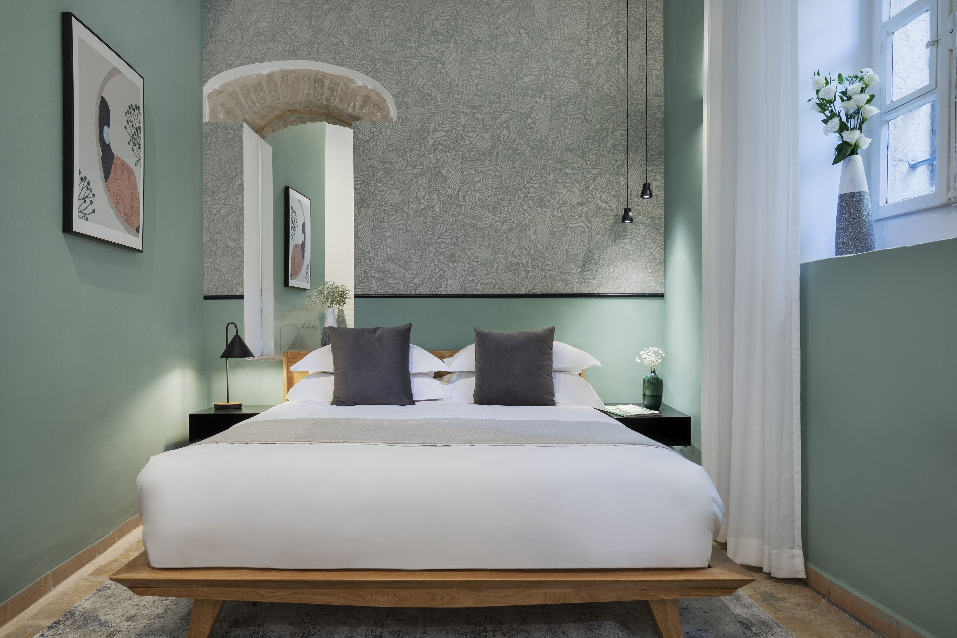 Una cama bien hecha con estructura de madera, una mesita de noche con lámpara y una pared con arte abstracto.