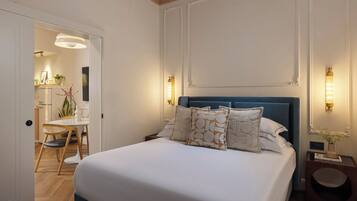 Un dormitorio ordenado con una cama grande, mesitas de noche y vista hacia la habitación contigua.