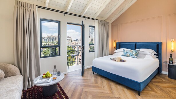 A spacious bedroom with a large bed, a balcony with a view of the city, and a dining area with a table and chairs. -  Villa Albi - Machne Yehuda Hotel (Jerusalem)