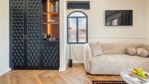 A living room with a sofa, a decorative cabinet, a window with a view, and a wall-mounted TV. -  Villa Albi - Machne Yehuda Hotel (Jerusalem)