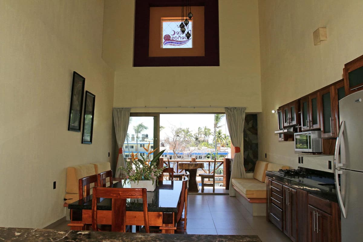 A spacious kitchen with wooden cabinets, a dining area with a table and chairs, and a large window with a view of palm trees.