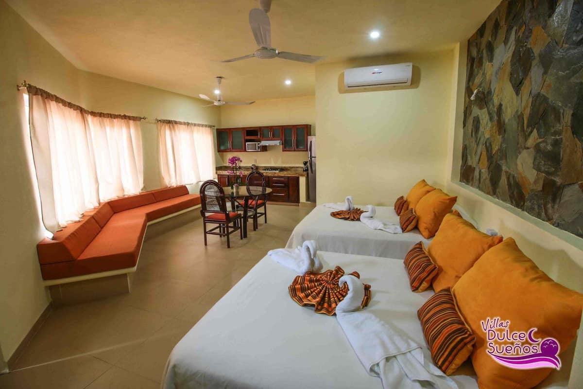 A hotel room with two beds, a dining area, and a kitchen.
