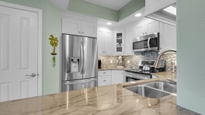 Una cocina moderna con armarios blancos, electrodomésticos de acero inoxidable, encimera de mármol y salpicadero con diseño de mosaico.