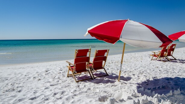 Una playa con sillas y sombrillas de playa rojas y blancas.