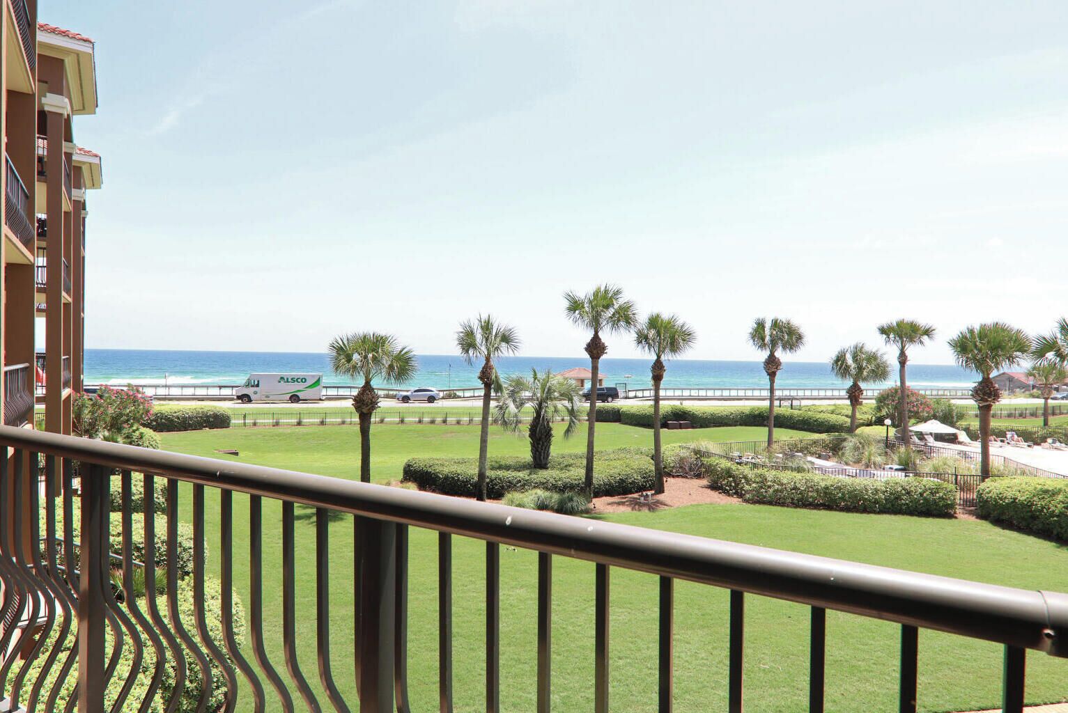 Un balcón con vistas al océano, palmeras y un campo de golf.