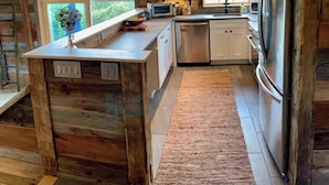 A rustic cabin-style kitchen with wooden walls, a large island, and a built-in refrigerator. - Remodeled Barn in Champlain Valley, Essex, NY (Essex)