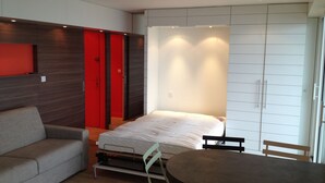 Een compacte kamer met een bed, een bank, een eettafel en een garderobe.