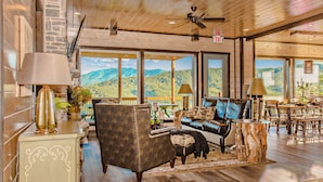 Un salon spacieux doté d’une grande fenêtre donnant sur un paysage montagneux, d’un parquet en bois et d’un mélange de meubles modernes et classiques.