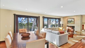 A spacious living room with a dining area, a fireplace, and large windows offering a view of the outside.