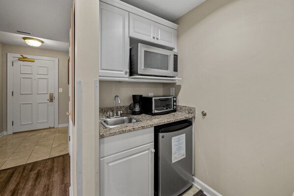 A compact kitchen with white cabinets, a microwave, a coffee maker, and a refrigerator.