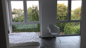 A modern bedroom with a bed, a chair, and large windows offering a view of greenery. - Kruft-apps (Kruft)