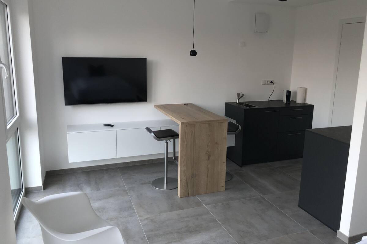 A modern kitchen with a wooden bar, a black island, and a large TV mounted on the wall.