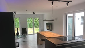 A modern kitchen with a wooden island, a glass dining table, and a TV mounted on the wall. - Kruft-apps (Kruft)