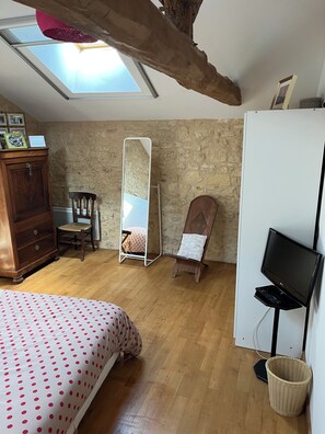 Quarto com cama, cómoda de madeira, espelho, cadeira, secretária com computador e televisão.