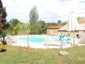 Piscina cercada, com cadeiras de descanso e um edifício de pedra ao fundo.