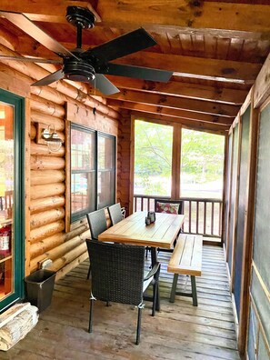 Una baita di legno con zona pranzo, tavolo e sedie, ventilatore a soffitto e ampie finestre.