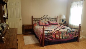 Una camera da letto con pavimento in legno, un letto con copripiumino floreale, due comodini, una cassettiera in legno e una finestra con tenda.