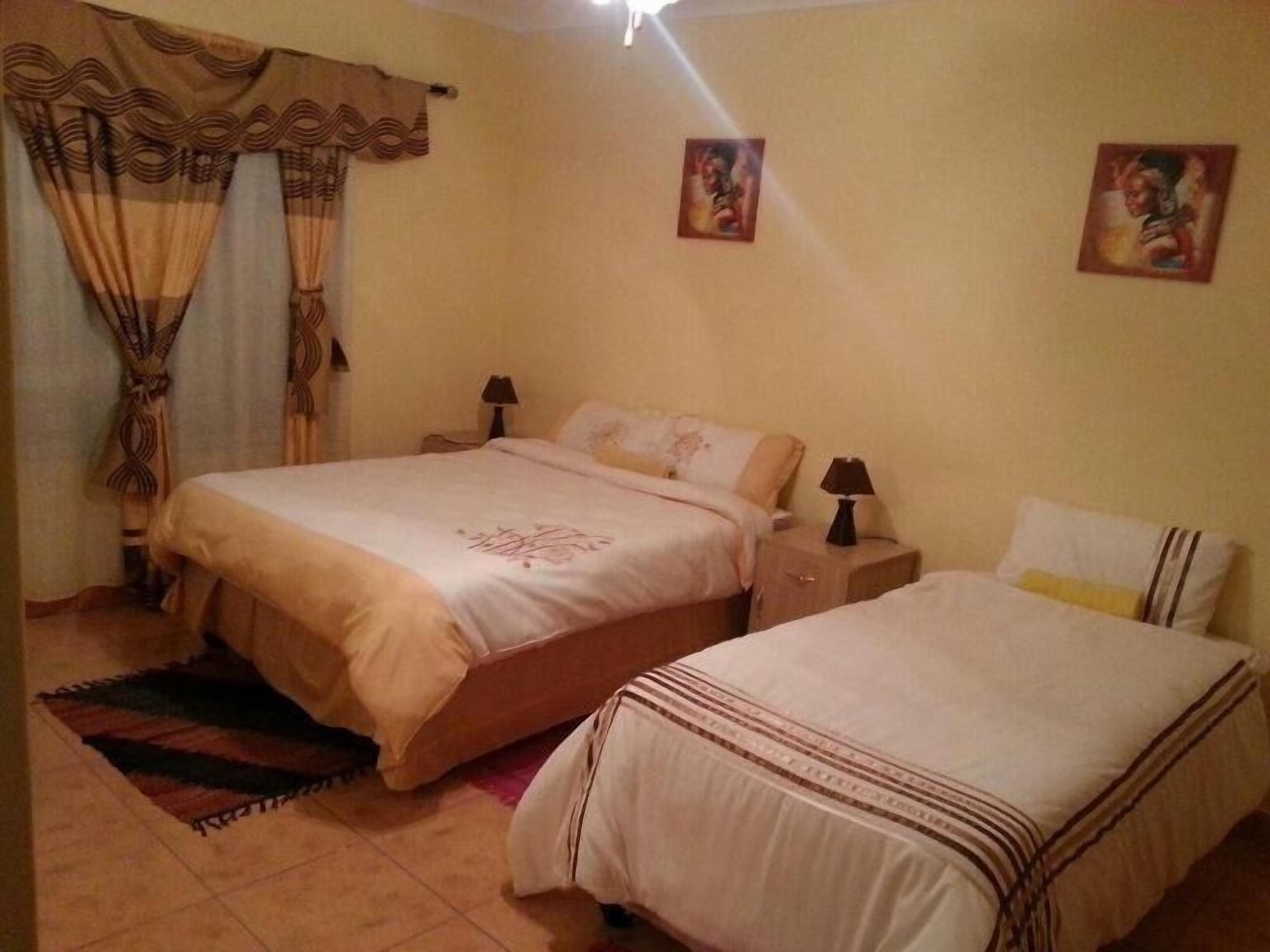 Ein Schlafzimmer mit zwei Betten, einem Nachttisch, einer Lampe und Vorhängen.