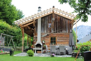A rustic wooden cabin with a stone patio, outdoor seating, and a chimney.
