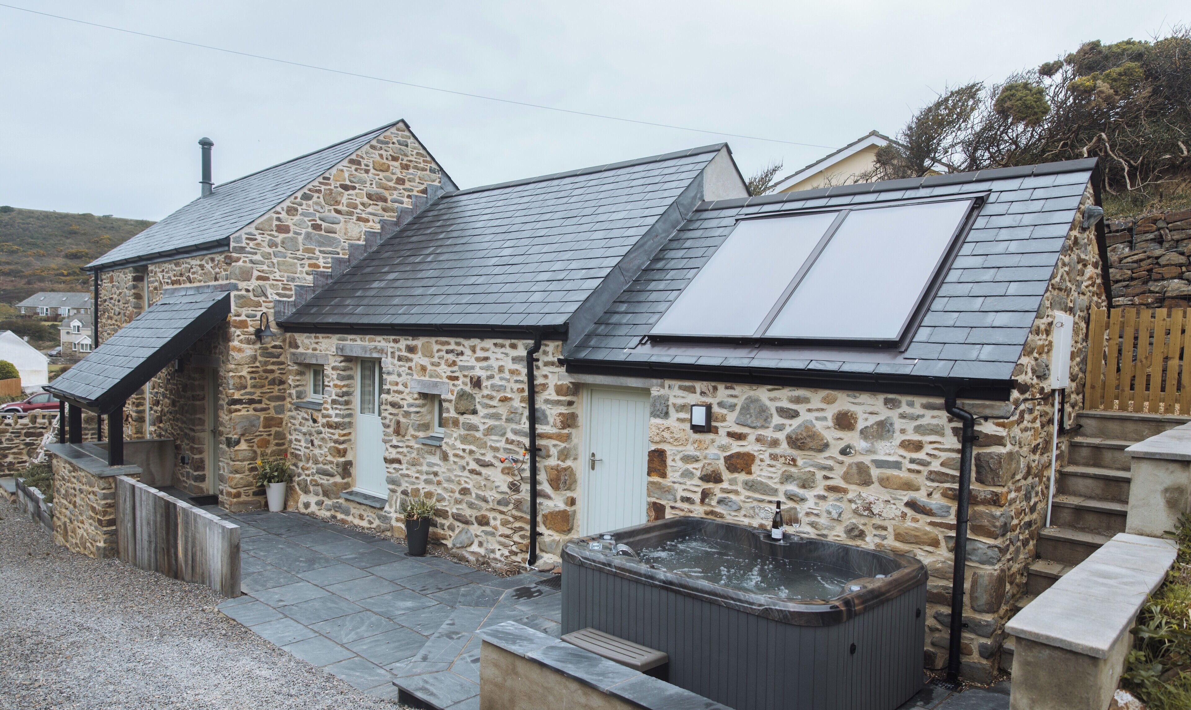 A stone building with a sloped roof, a hot tub, and a small staircase leading to a door.