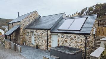 A stone building with a sloped roof, a hot tub, and a small staircase leading to a door.