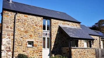 A stone building with a sloped roof, a small window with shutters, and a wooden fence in front.