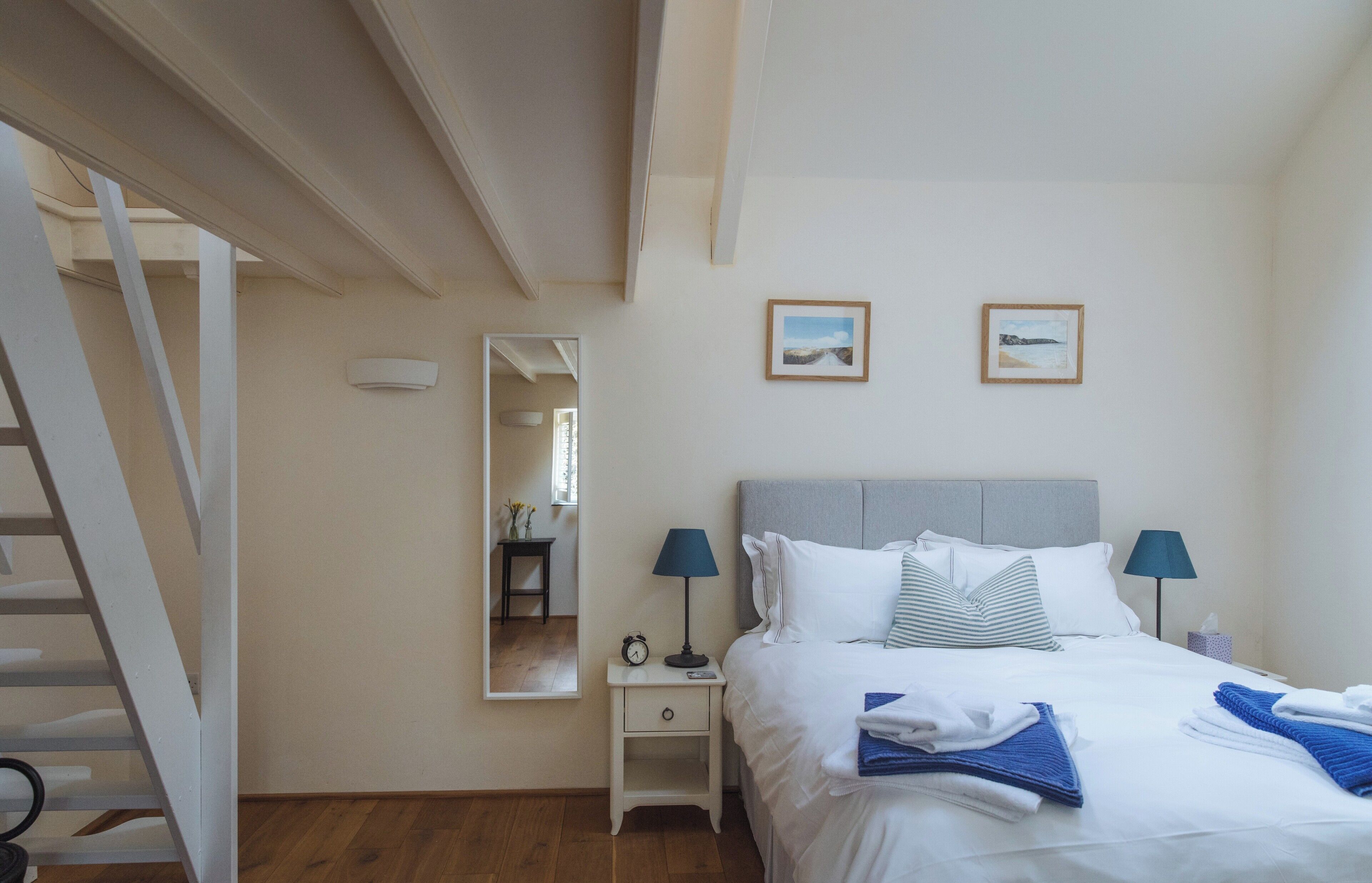 A bedroom with a bed, two bedside lamps, a nightstand, a mirror, and two framed pictures on the wall.