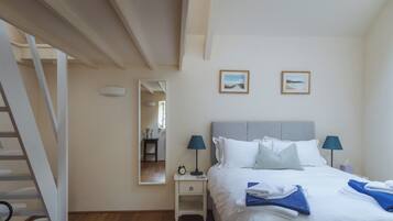 A bedroom with a bed, two bedside lamps, a nightstand, a mirror, and two framed pictures on the wall.