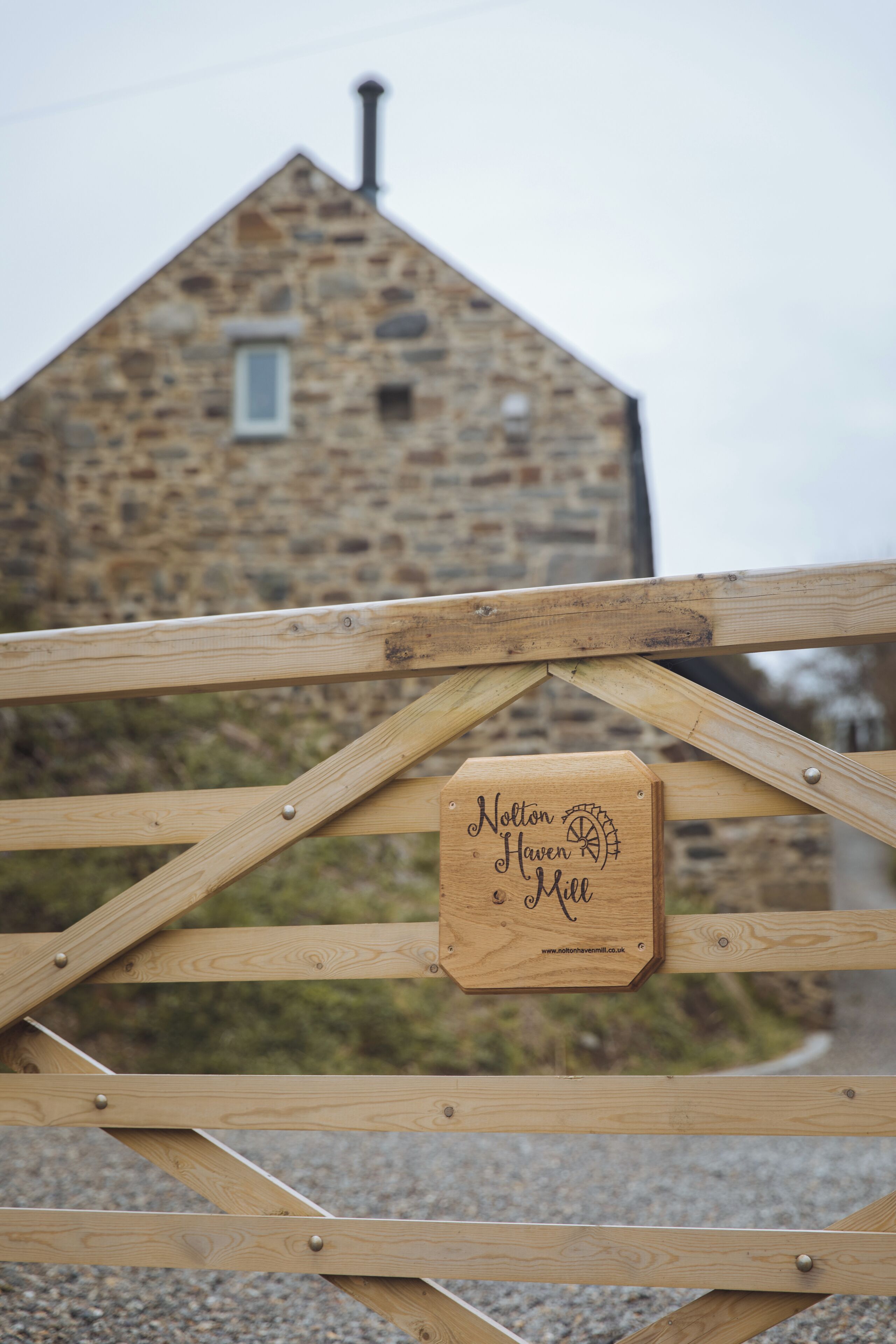 A wooden gate with a plaque reading "Nolton Haven Mill."