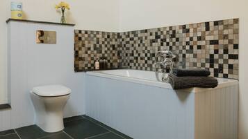 A bathroom with a toilet, a bathtub with a shower, and a mosaic tile wall.