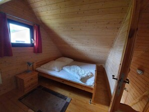 Ein kleines Zimmer mit einem Einzelbett, Holzwänden und einer geneigten Decke.