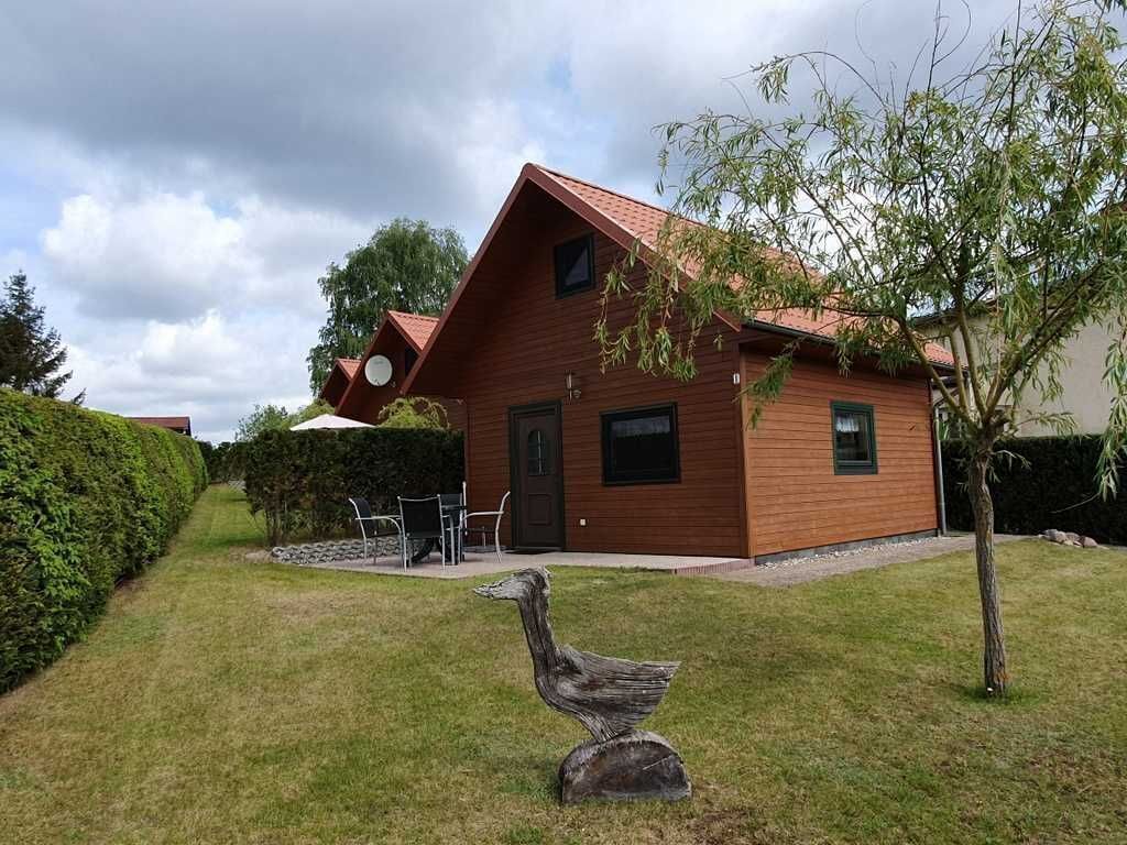 Une maison en bois avec un toit en pente, un petit porche à l’avant et une sculpture d’oiseau dans le jardin.