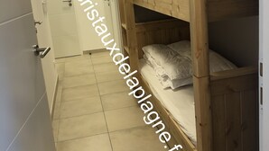 Un estrecho pasillo con una litera de madera apoyada en la pared, una puerta con manija y un piso de baldosas.