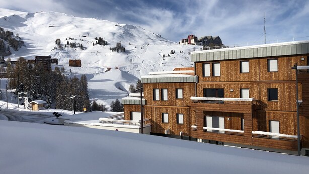 Un edificio moderno con fachada de madera, situado en una zona montañosa nevada.